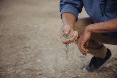 一个人蹲下来，手里拿着一把沙子，沙子从手指间滑过